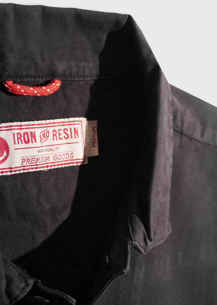 Close-up of a black shirt collar with a red loop and "Iron and Resin" label, indicating premium quality and medium size.