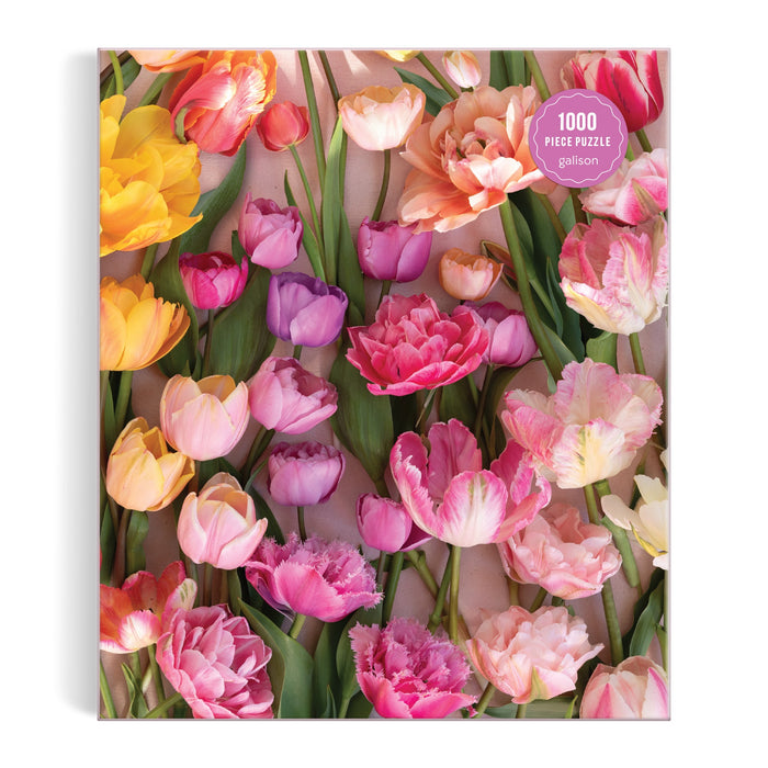 The Ephemeral Tulips 1000 Piece Puzzle by Christine Chitnis features vibrant yellow, pink, purple, and peach tulips with lush green leaves on a light background—ideal for eco-friendly puzzlers.