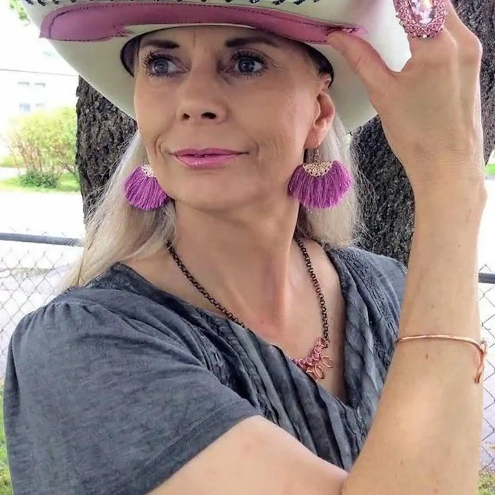 Woman wearing a stylish cowboy hat, purple earrings, and jewelry, showcasing a confident expression outdoors.