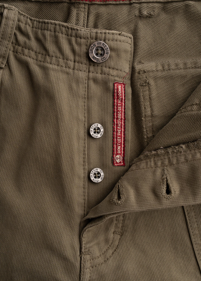 Close-up of khaki pants with metal buttons and red stitching detail, featuring text "Don't let the bastards get you down."