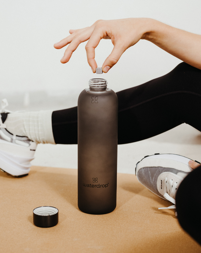 Person holding a frosted glass water bottle made of robust borosilicate glass, designed for long-lasting use.