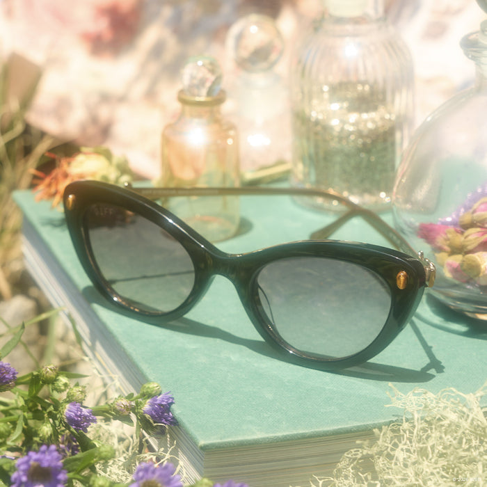 still life - diff eyewear x practical magic 2 gillian cateye sunglasses laying on a book outdoors