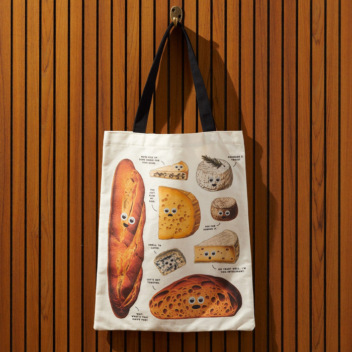 The Brass Monkey Googly Food Canvas Tote features whimsical bread and cheese artwork with playful labels, making it the perfect accessory to add foodie flair to your everyday outings.