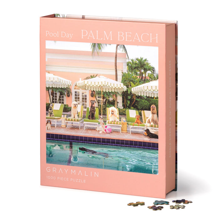 The Gray Malin Pool Day Palm Beach 1000 Piece Book Box Puzzle features dogs relaxing poolside at The Colony Hotel, with pastel umbrellas and palm trees—an ideal gift for dog fans and puzzle lovers.