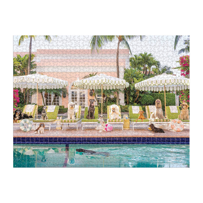 Dogs of all breeds relax on poolside chairs under striped umbrellas by a sparkling pool, with palm trees and The Colony Hotel—capturing the vibrant, summery fun of the Gray Malin Pool Day Palm Beach 1000 Piece Book Box Puzzle by Gray Malin.