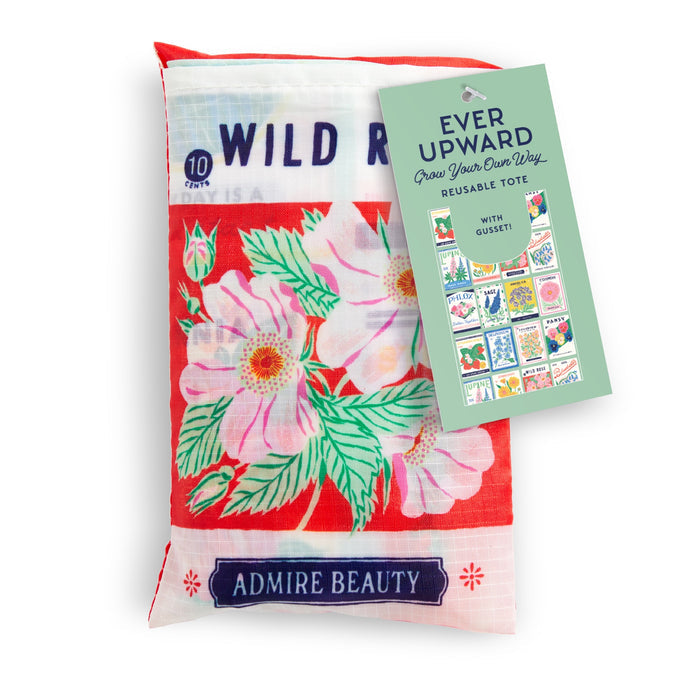 The Grow Your Own Way Packable Nylon Tote Bag by Emily Taylor features eco-friendly red nylon with pink and white wild roses, green leaves, and a tag reading “Ever Upward—Reusable Tote” and “ADMIRE BEAUTY.” Conveniently folds for easy packing.