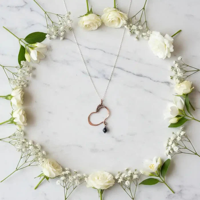 Hammered Copper Butterfly Wing Child Abuse Survivor Necklace with black Swarovski crystal pendant, surrounded by white flowers.