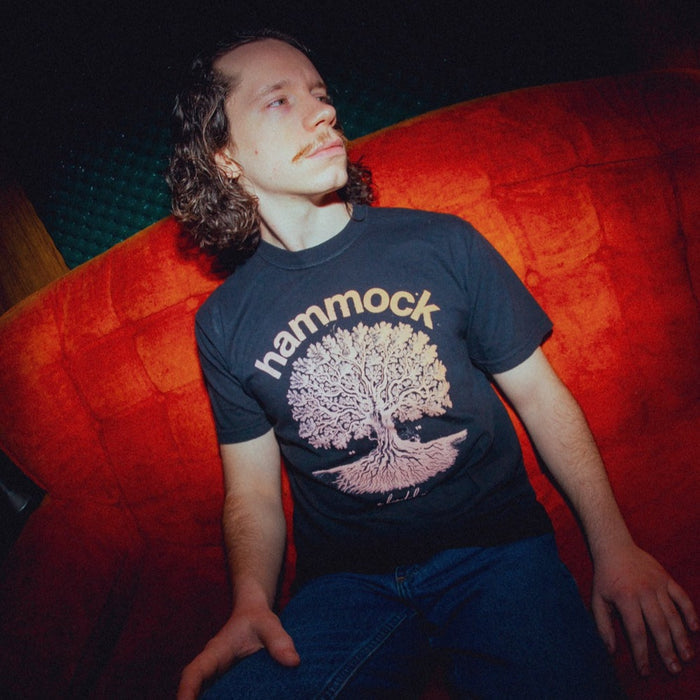Photo of a man wearing the shirt. He is sitting on an orange sofa.