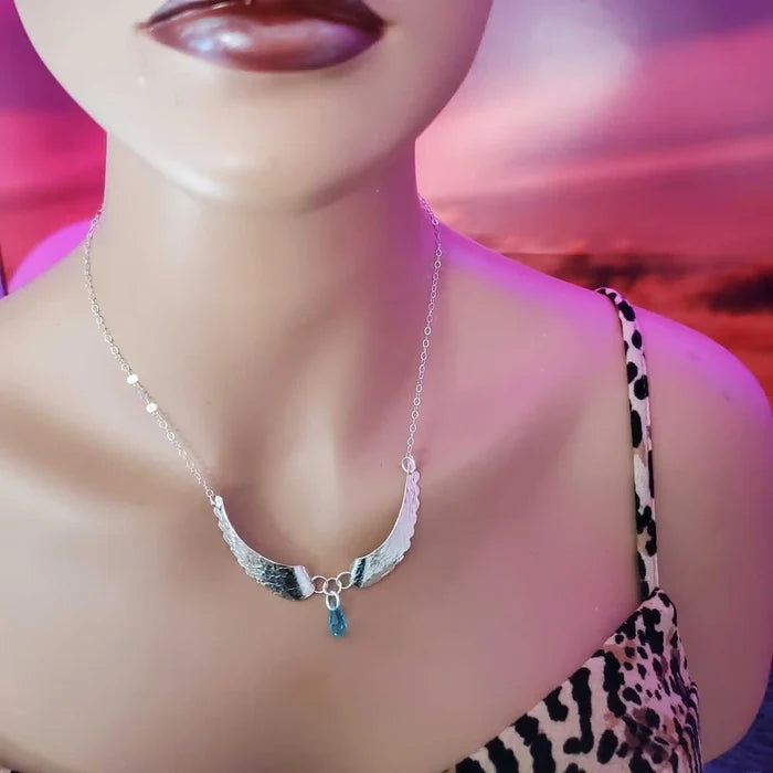 Handmade Silver Forged Sculpted Angel Wings Necklace worn on a mannequin against a colorful background.