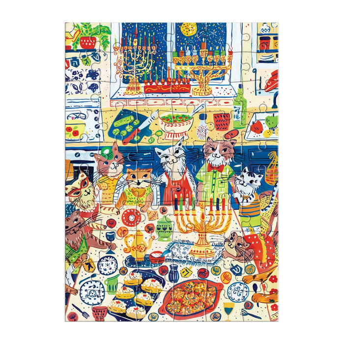 The Happy Hanukcats Greeting Card Puzzle by Anna Ivanir features festive felines in sweaters celebrating Hanukkah in a kitchen with menorahs, dreidels, decorations, and holiday treats on a snowy night.