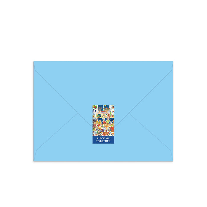 A closed light blue envelope with a festive feline sticker and the text PIECE ME TOGETHER holds the Happy Hanukcats Greeting Card Puzzle by Anna Ivanir—an interactive Hanukkah card with a playful cat-themed puzzle inside.