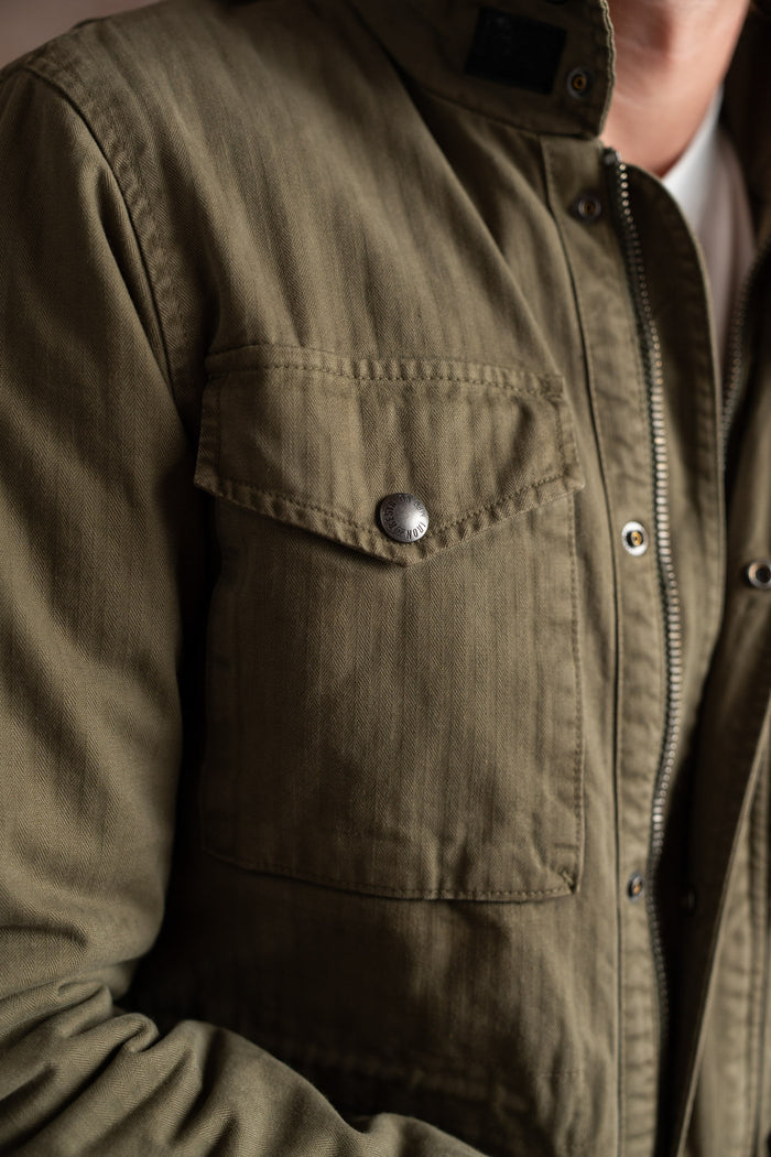 Close-up of a person wearing a green jacket with a buttoned pocket and zipper, highlighting the texture and design details.