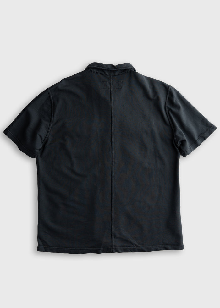 Back view of a black short-sleeve shirt on a plain background, highlighting its simple design and straight seam down the center.