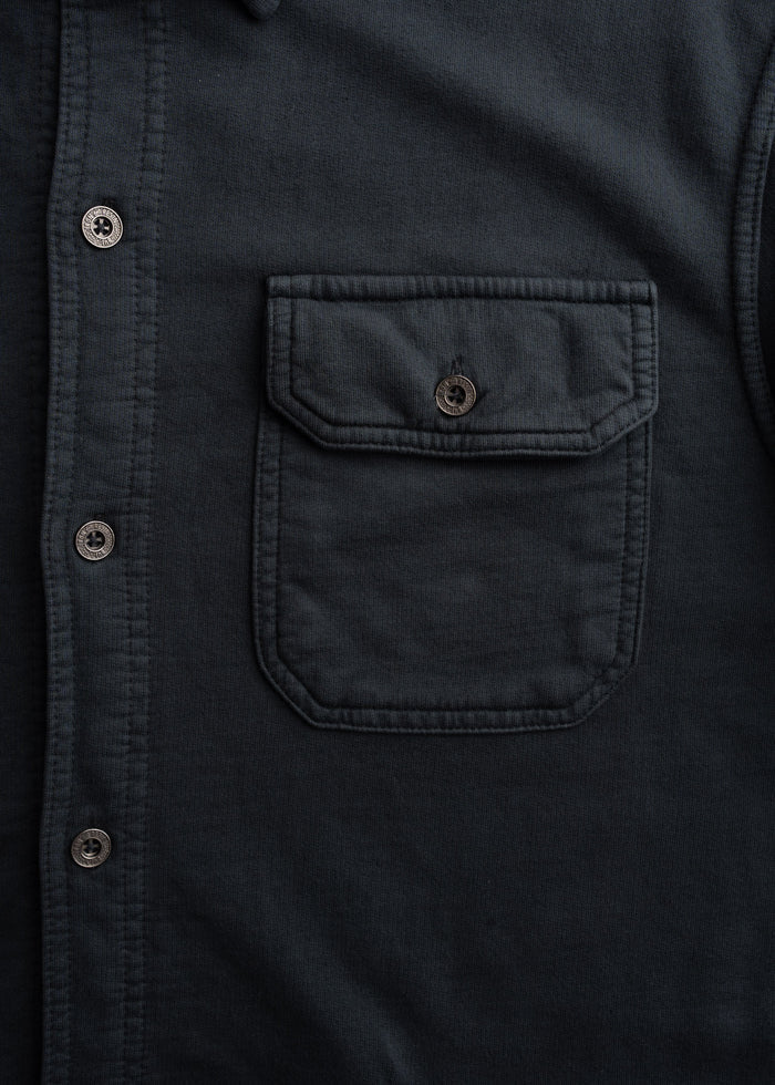 Close-up of a dark shirt with a buttoned pocket and row of buttons, highlighting its texture and design details.
