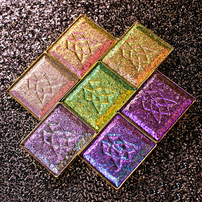 Dimensional Multichrome Eyeshadows laying on a back sparkly background.