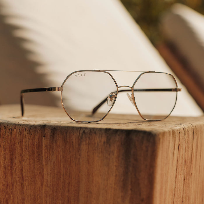 still life - jojo fletcher x diff eyewear joelle navigator sunglasses with a gold metal and chocolate crystal temples with grey tinted lenses laying on a table
