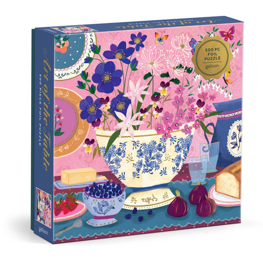 The Joy Laforme Art of the Table 500 Foil Piece Puzzle features a colorful floral tea table scene with flowers, fruit, butter, and bread against a pink background. Brand: Joy Laforme.