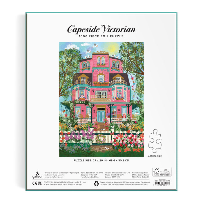 Back of the Joy Laforme Capeside Victorian 1000 Piece Foil Puzzle box features a vibrant illustration of a pink Victorian mansion with balconies, lush trees, and a white picket fence with flowers. Brand: Joy Laforme.