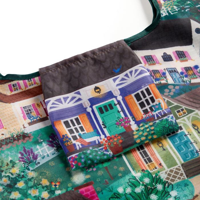 A close-up of the Joy Laforme Cottage Hills Packable Nylon Tote Bag, featuring cottage artwork with porches and colorful doors in teal, orange, and purple—crafted from eco-friendly materials and includes a handy pocket.