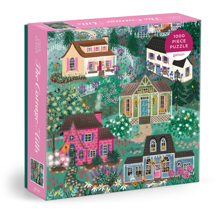 The Joy Laforme The Cottage Hills 1000 Piece Puzzle, by Joy Laforme, features five whimsical cottages amid lush gardens with pink and green floral accents, packaged in a square box.