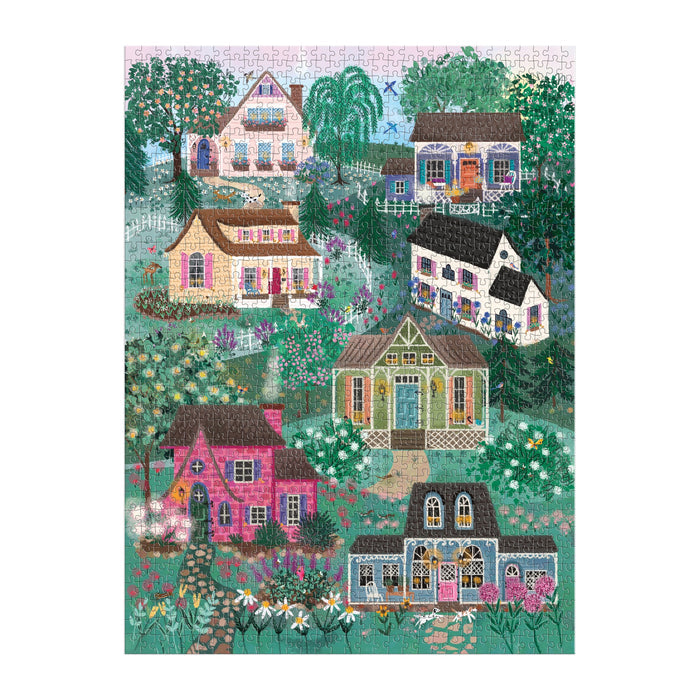 The Joy Laforme The Cottage Hills 1000 Piece Puzzle in a Square Box by Joy Laforme features whimsical houses and lush greenery on a sloping hillside, perfectly capturing the charm of idyllic suburban living.