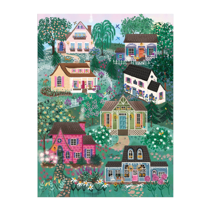 The Joy Laforme The Cottage Hills 1000 Piece Puzzle features a vibrant, whimsical village scene with seven charming houses, lush trees, and flowers, capturing idyllic suburban life. Enjoy this cozy puzzle by Joy Laforme in a square box.