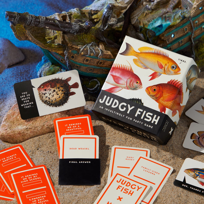 The Judgy Fish Game by Brass Monkey features illustrated fish on the box and colorful cards, including playful insult cards like “You are not wrong for thinking that” and “Dead Vessal,” perfect for fun parties.
