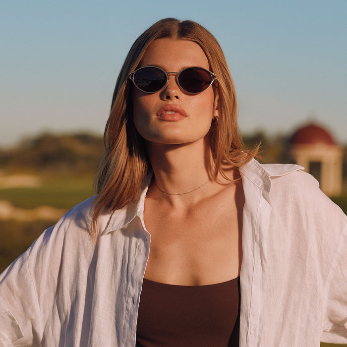 lifestyle - female at a country club wearing diff eyewear juliette round sunglasses with a brush gold metal frame and truffle brown polarized lenses front view