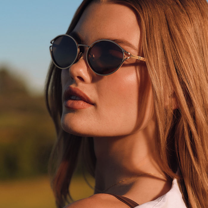 lifestyle - female at a country club wearing diff eyewear juliette round sunglasses with a brush gold metal frame and truffle brown polarized lenses angled view