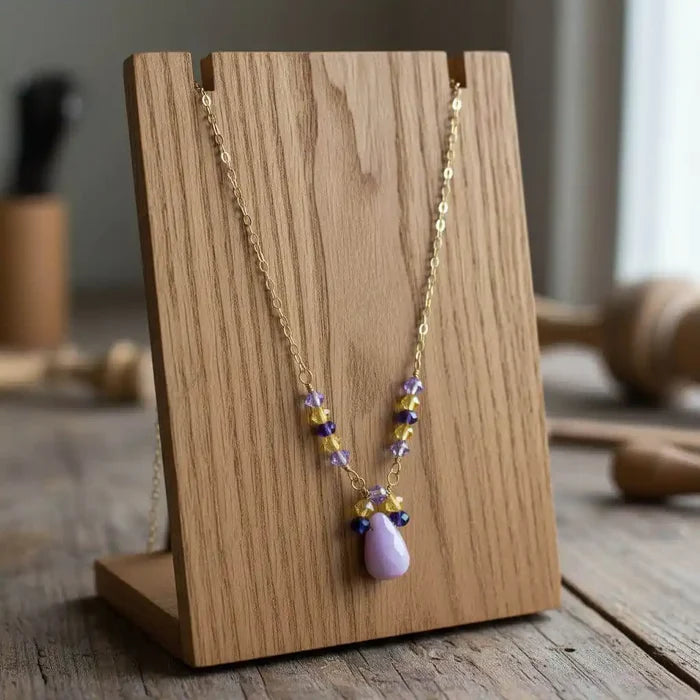 Lavender Candy Jade Drop Gold Wire Wrapped Necklace displayed on a wooden stand, showcasing its lavender-pink pendant and Swarovski accents.