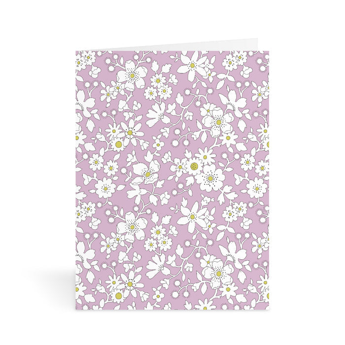 The Liberty Floral Greeting Assortment Notecard Set Volume 2 by Liberty of London Ltd features a light purple card adorned with white and yellow flowers and green leaves—a charming addition to any greeting card collection.