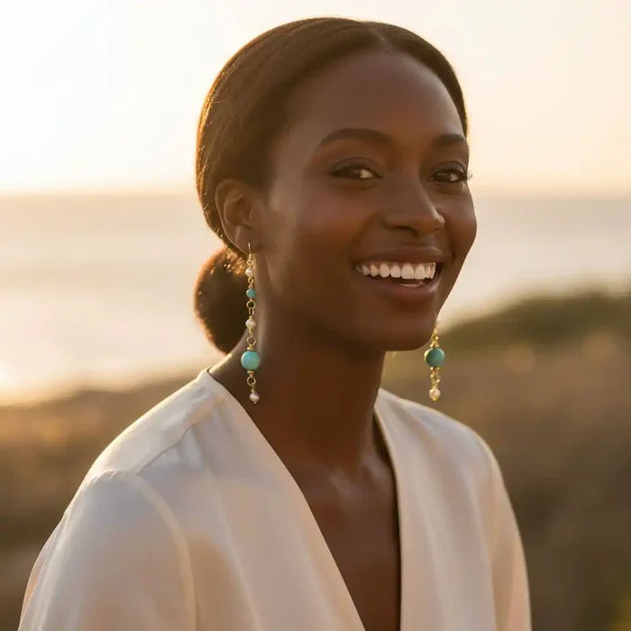 Woman smiling while wearing Long 14 K Gold Filled Turquoise Pearl Earrings against a scenic backdrop.