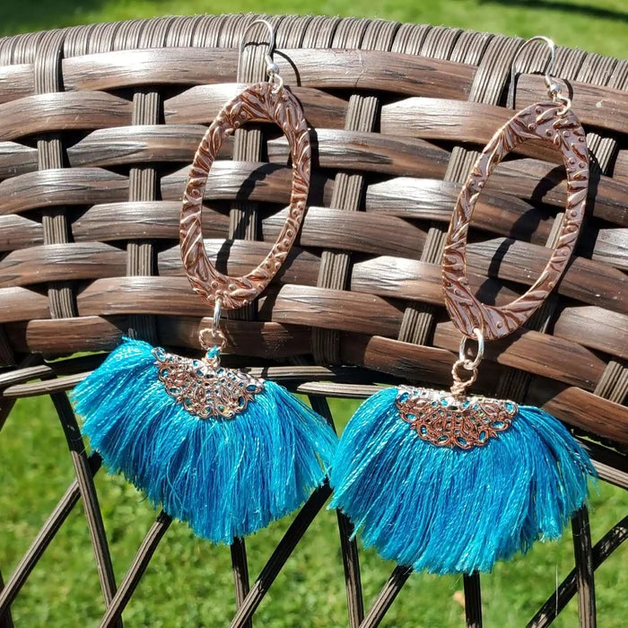 Long Copper Embossed Aqua Brushed Silk Fan Tassel Earrings displayed against a wicker background.