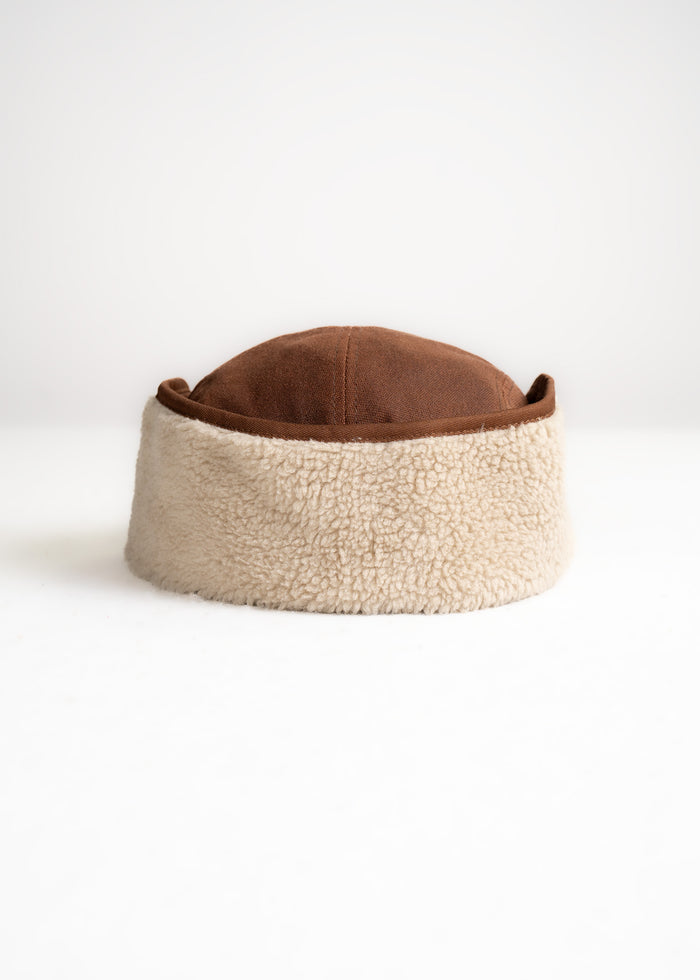 Brown suede hat with beige shearling lining on a white background, showcasing its cozy and stylish design.