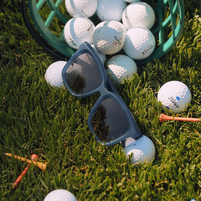 still life - golf balls and tees resting with diff eyewear featuring the meredith square oversized sunglasses with a clubhouse blue acetate frame and grey gradient polarized lenses