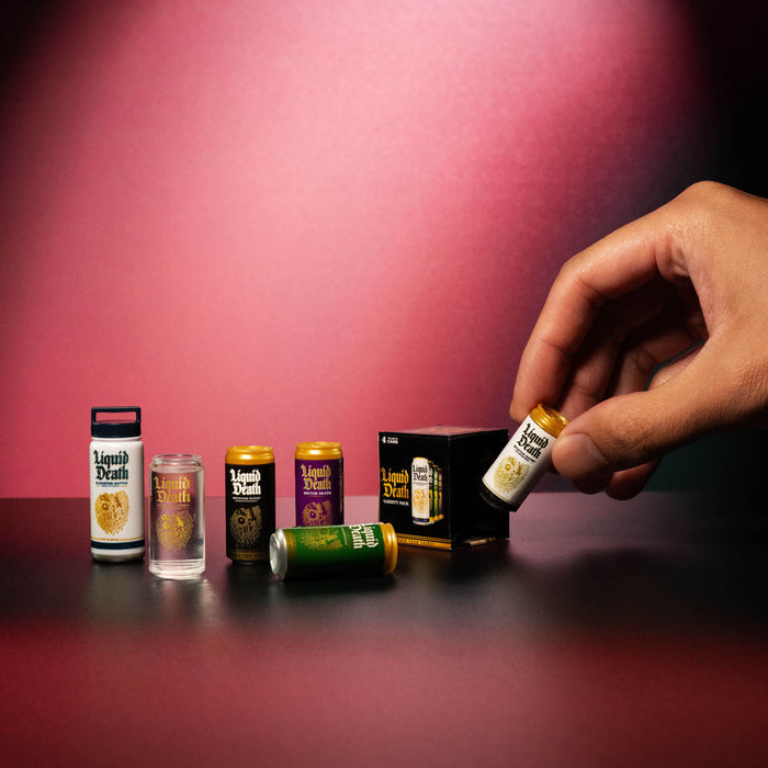Hand holding a Liquid Death product with various other products on a red surface and background.