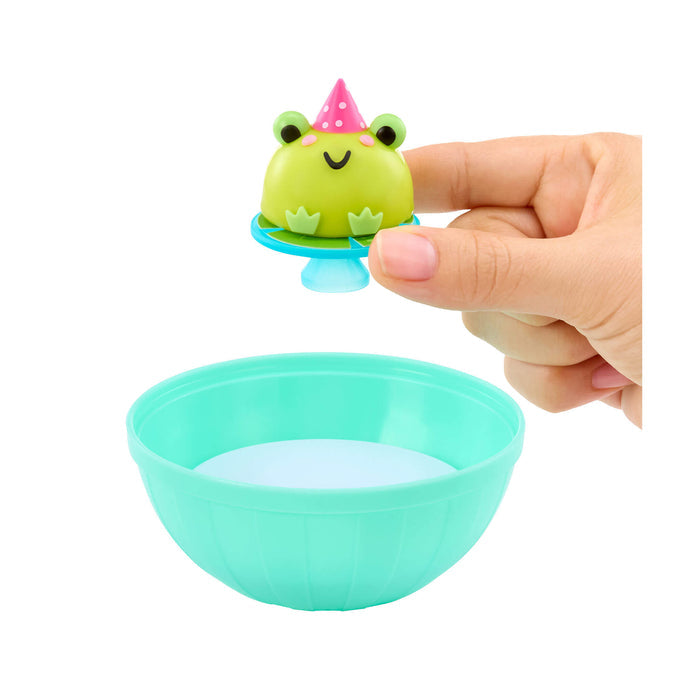 Small green frog toy with a pink party hat on top of a teal bowl held by a hand.
