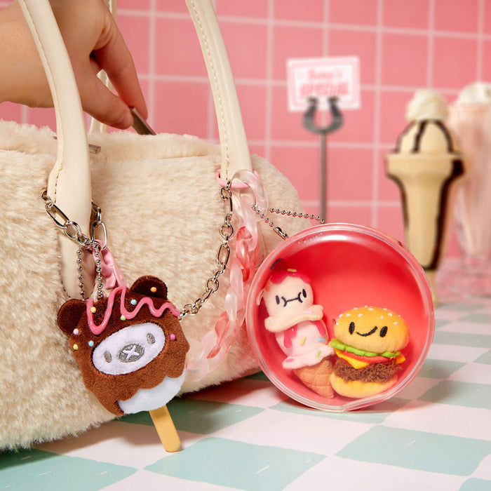 Keychain with ice cream and donut design held by a hand, with a pink background.