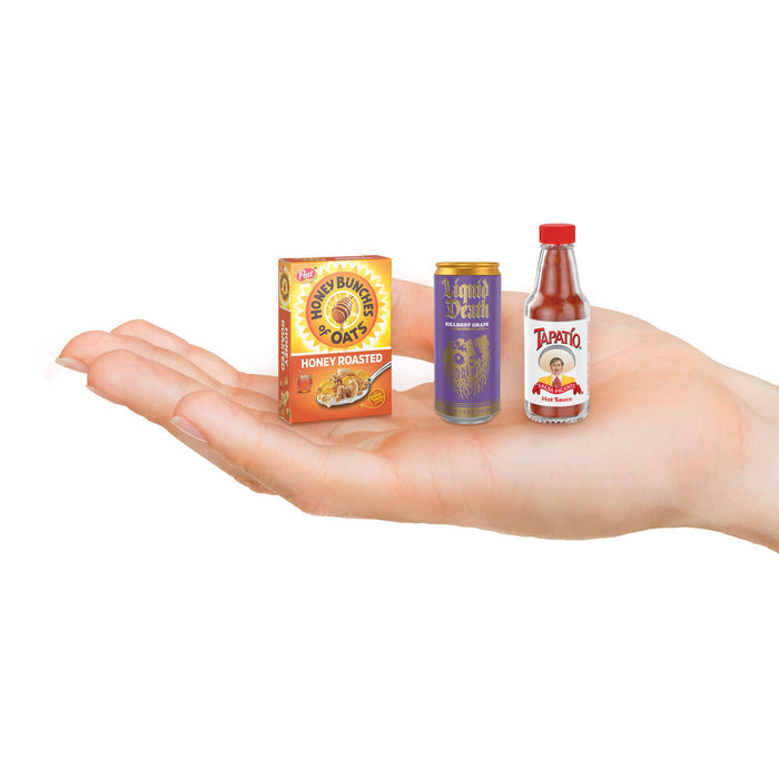 Miniature packages of Honey Bunches of Oats, Lipton Iced Tea, and Tapatio hot sauce held in a hand on a white background.