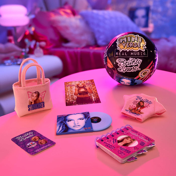 Collection of Britney-themed merchandise including a ball, mini album, and tote bag on a pink surface.