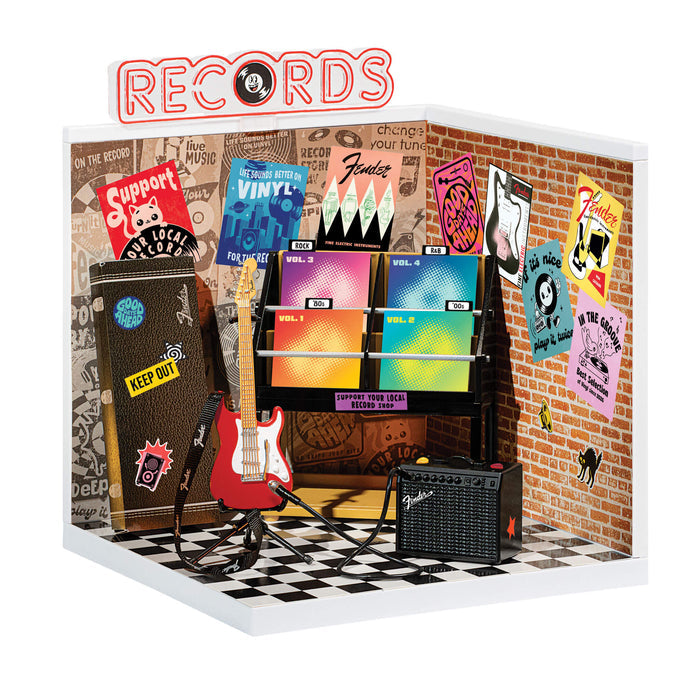Miniature record store display with vinyl records, guitar, and amplifier against a brick wall.