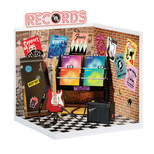 Miniature record store display with vinyl records, guitar, and amplifier against a brick wall.