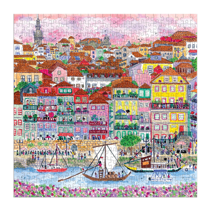 The Michael Storrings Colors of Porto 500 Piece Puzzle by Michael Storrings features a vibrant European riverside scene with red-roofed buildings, boats, people on the quay, and a pink-purple sky.