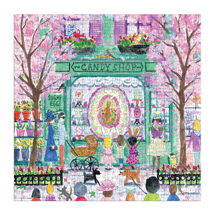 The Michael Storrings Easter Candy Shop 500 Piece Puzzle depicts a vibrant candy store scene with blooming trees, flowers, and families admiring the display—perfect for puzzle fans.