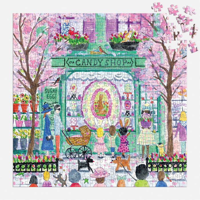 The Michael Storrings Easter Candy Shop 500 Piece Puzzle by Michael Storrings features a vibrant shop scene with flowers, people, children, and two rabbits at the entrance; several loose pieces remain in the upper right corner.