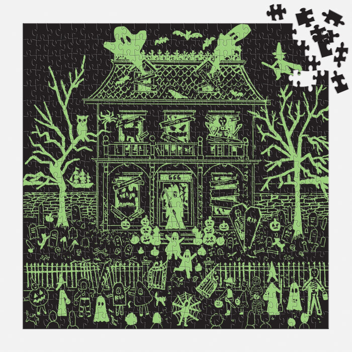 The Michael Storrings Haunted House 500 Piece Glow in the Dark Puzzle, by Michael Storrings, depicts a haunted house with ghosts, skeletons, eerie trees, and gravestones. A few pieces are missing from the upper right; the image glows green in the dark.