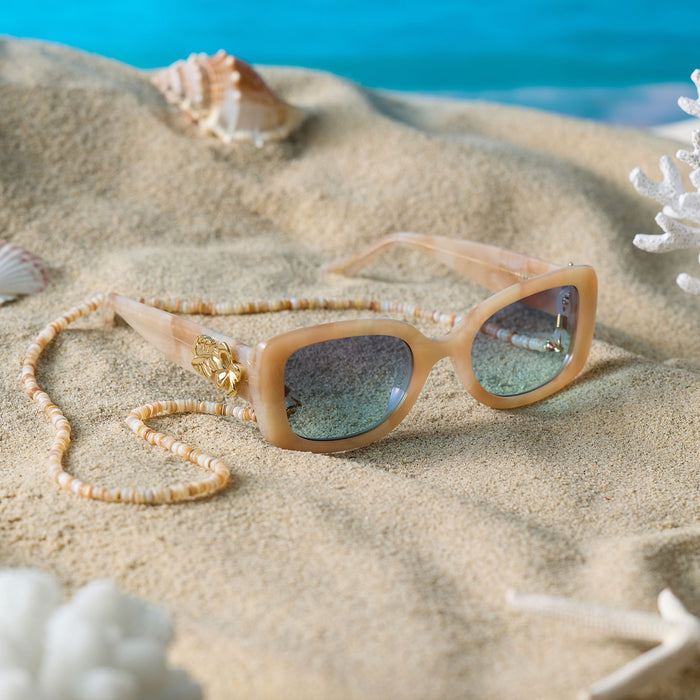 still life - diff eyewear x disney princess featuring the moana square sunglasses with a beige tortoise acetate frame and seafoam green lenses angled view laying on a beach