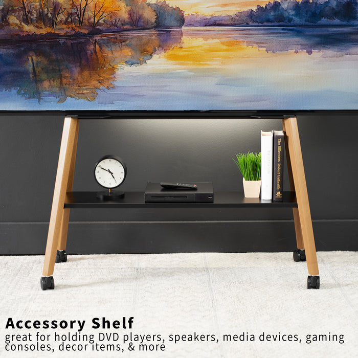 A black accessory shelf with walnut wood legs and black casters, shown holding a console, books, and a small plant in a room setting under a landscape painting.