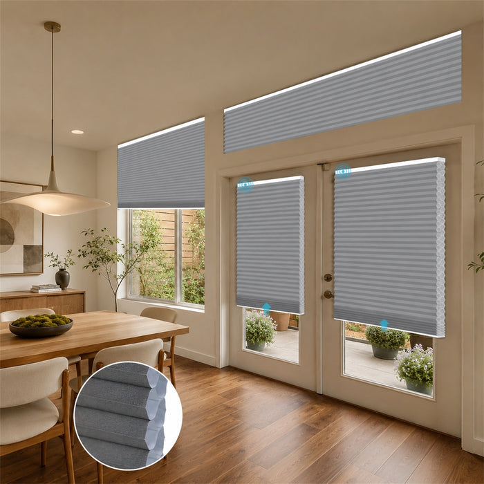 Gray cellular window and door blinds installed in a modern dining room and patio area, with an inset circular detail of the fabric texture.