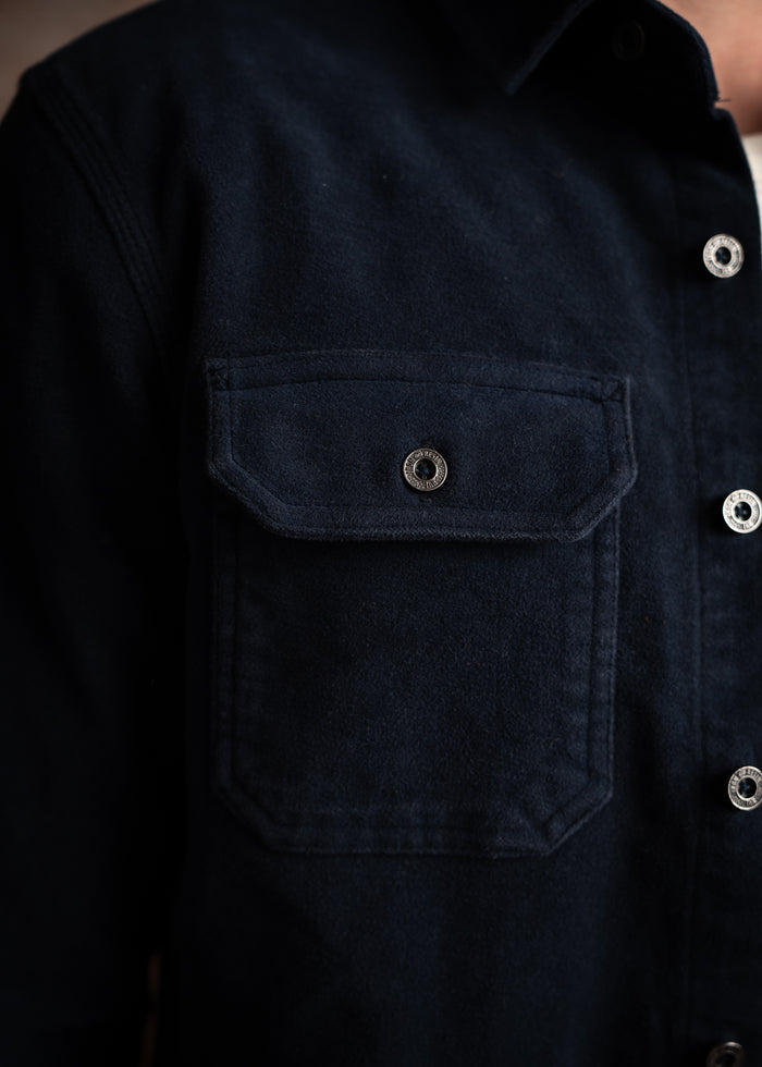 Close-up of a navy blue shirt with a buttoned flap pocket, highlighting its texture and details against a soft background.